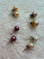All four pairs of pearl stud earrings laid out on white fabric