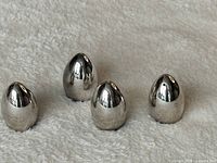 Four polished stainless steel egg-shaped shakers upright on fabric surface
