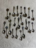 Front view of 22 assorted souvenir spoons laid out on white background
