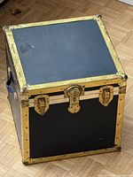 Full view of square black trunk with brass hardware