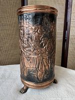 Full front view of cylindrical copper umbrella stand showing embossed tavern scene and paw feet