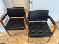 Front view of both armchairs showing wood frames and black tufted cushions