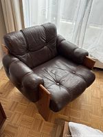 Front view of brown leather armchair showing button-tufted cushions and wood sides