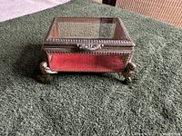 Angled closed view of glass trinket box showing frame and cherub feet