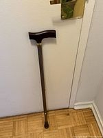 Full view of cane leaning against wall showing handle, shaft and tip