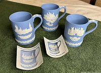 Front view of the three blue jasperware mugs with relief buildings and leaflets