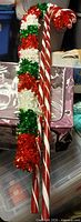 Two plastic candy cane yard stakes and several red, white, green tinsel garlands leaning together