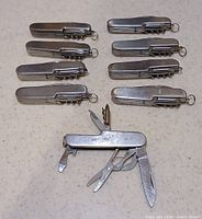 Seven closed and one opened stainless steel multi-tool pocket knives showing included tools