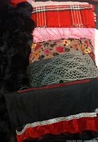 Stack showing multiple scarves including black faux fur, red tartan, pink paisley, floral tapestry, grey knit, black with red ruffle