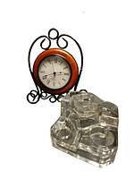 Clock on metal scroll stand beside pressed glass holder