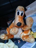 Front view of oversized orange-tan Pluto plush with white belly, black ears and nose