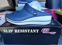 Left side view of navy Skechers Work clog on top of original box