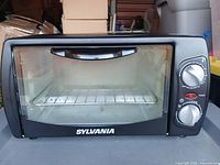 Front view of Sylvania toaster oven showing glass door, brand name and control knobs