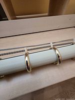 Full view of curtain rod showing ribbed white surface, gold rings and chain