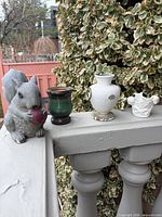 Group shot of squirrel, wooden pot, ceramic vase and cherub planter on railing