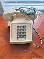 Front view of beige wall phone with keypad and cords