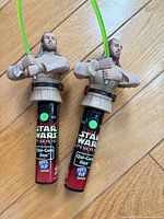 Front view of both Qui-Gon Jinn Spin Pop dispensers showing figures, lightsabers and handles