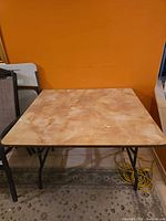Overall view of square folding table against orange wall
