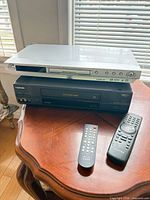 JVC DVD player stacked on Toshiba VHS player with two remotes