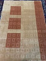 Full view of rectangular beige and rust-brown rug with square pattern