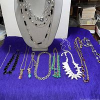 All nine necklaces displayed together on purple cloth and bust