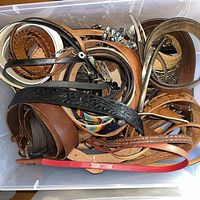 Overview of tote filled with belts showing variety of colors, textures and buckle styles