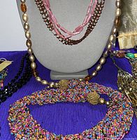 Group of six assorted beaded and chain necklaces displayed on bust and table