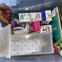 Tub containing unused foam insoles, boxed foot care products, red wedge sandal and bagged accessories