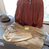 Rust suede bomber, tan suede blazer, grey wide-brim hat grouped on table