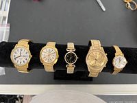 All five gold-tone wristwatches on display stand