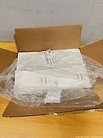 Closed cardboard box opened to reveal fan-fold label stack wrapped in plastic