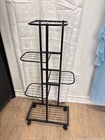 Assembled example of the black metal foldable plant stand showing full height and four shelves