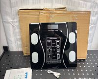 Scale on table in front of two cardboard boxes with manual and USB cable visible