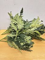 Pile of eight green artificial fern stems on table