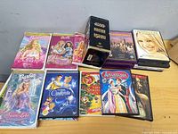 Overall view of DVDs and VHS tapes including Barbie titles, Star Wars box, assorted stacks