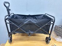 Full view of assembled black folding wagon showing frame, fabric basket, handle and wheels