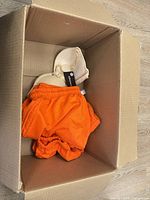Box with orange shorts and off-white top showing tags
