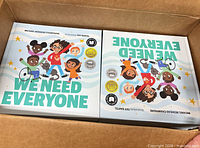 Top view of open case showing stacks of identical "We Need Everyone" books