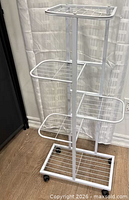 Front view of assembled white metal plant stand on casters