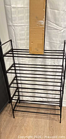 Assembled black multi-tier metal shoe rack beside sealed box