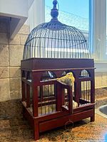 Full view of bird cage showing wood base, metal dome, finial, faux birds