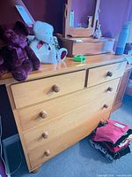 Front view of light wood dresser showing five drawers and knobs