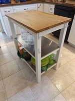 Three-quarter view of cart showing oak top, white frame, stainless shelves, casters