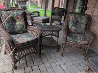 Pair of rattan armchairs with floral cushions flanking matching glass-top side table