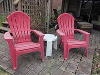 Pair of red plastic Muskoka chairs with white round table on patio