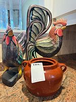 Two carved wooden roosters and brown ceramic bean pot on countertop