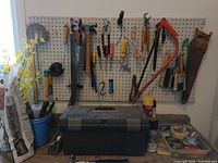 Overall view of pegboard with assorted hand tools, toolbox, polymeric sand bag, spray foam