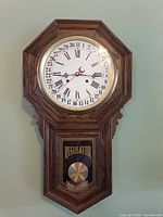 Front view of octagonal regulator wall clock showing full case and lower glass panel