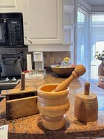 Three wooden kitchen tools on countertop: rectangular butter press, cylindrical butter mold, mortar with pestle