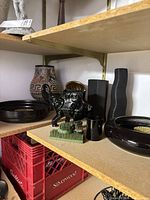 Shelf view showing multiple black ceramic vessels, terracotta vase, brass pots, flower frog